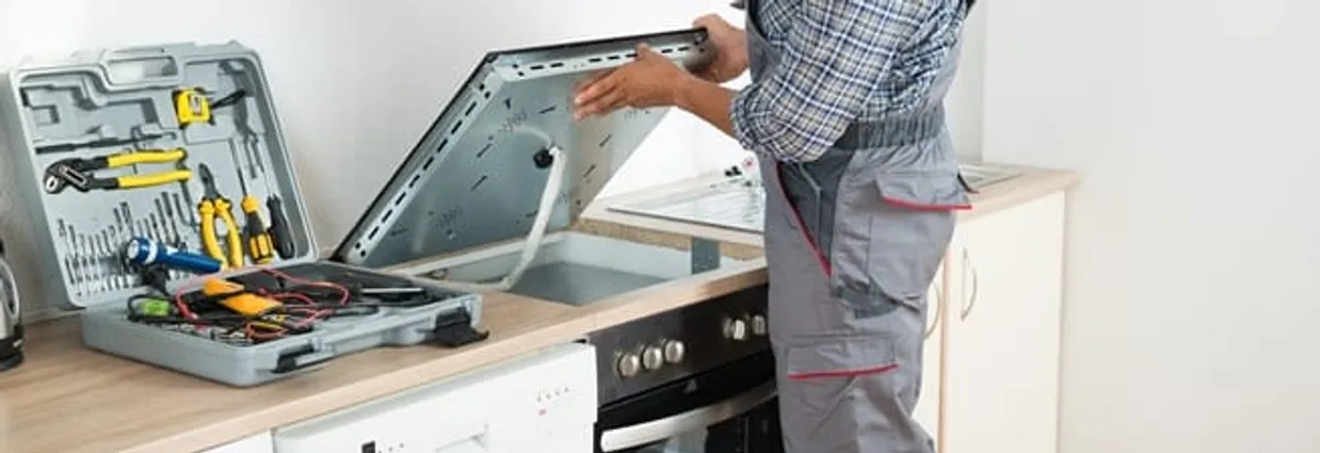 Cooktop repair technician lifting a built-in stovetop for service in Peoria, IL
