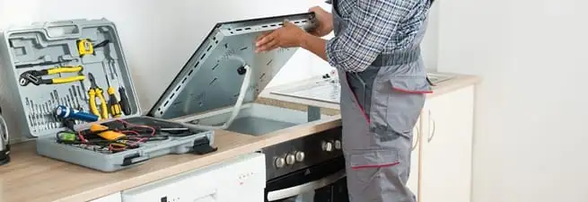 Cooktop repair technician lifting a built-in stovetop for service in Peoria, IL