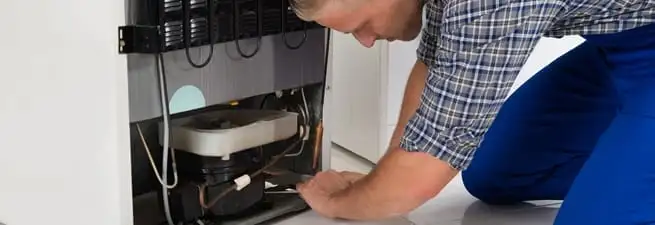 Refrigerator repair technician servicing the compressor and condenser area in Peoria, IL