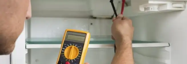 Refrigerator repair technician testing electrical components with a multimeter in Peoria, IL