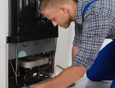 Refrigerator repair technician servicing the compressor and condenser area in Peoria, IL